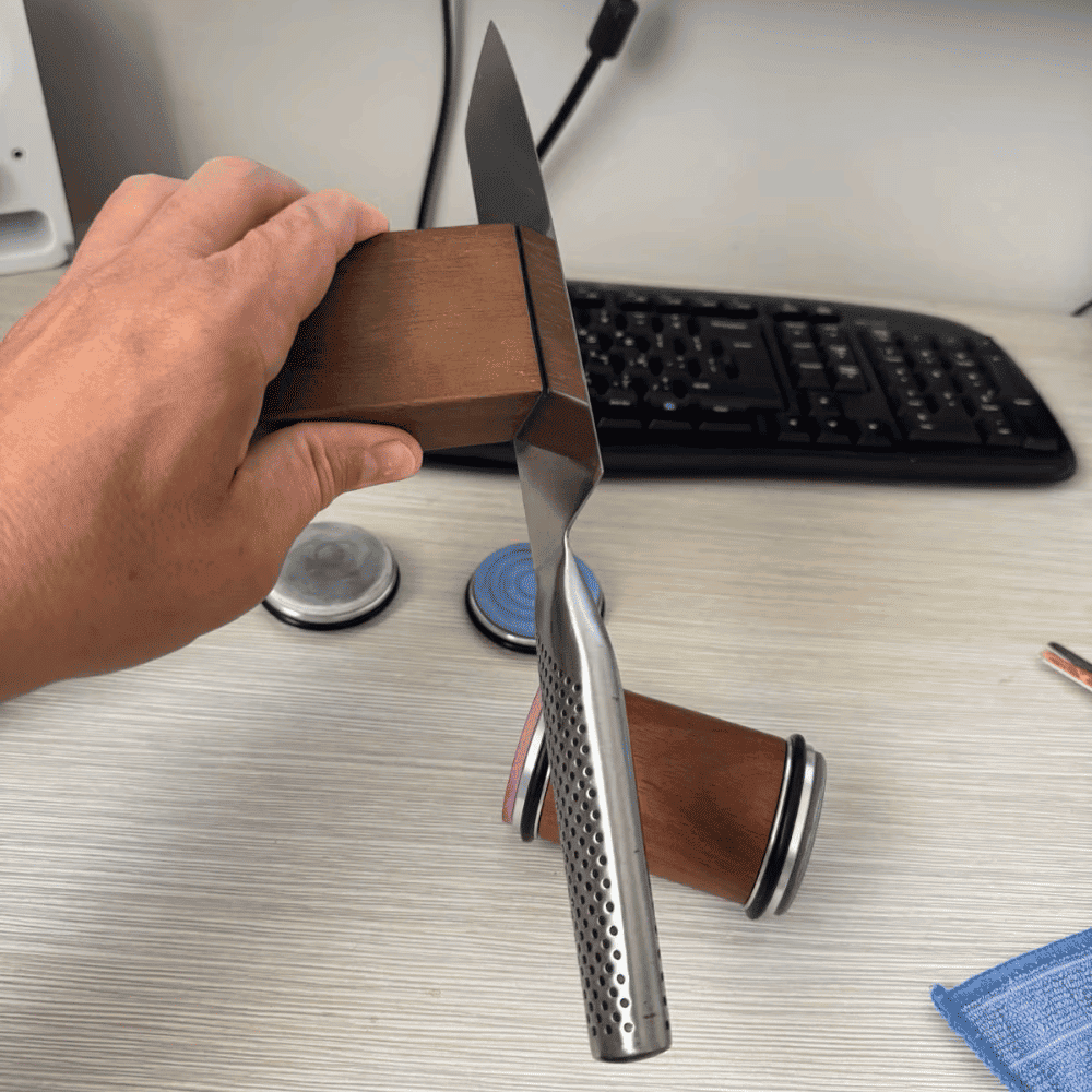 Hand holding a knife with a wooden handle on a desk with a keyboard and office supplies.